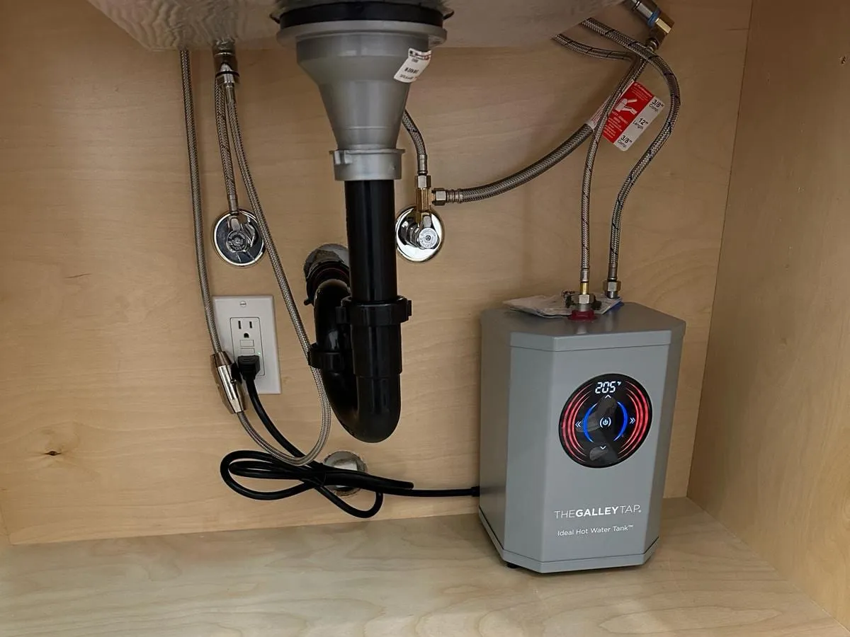 An under-sink instant hot water tank with a digital temperature display, connected beside the sink drain and supply valves