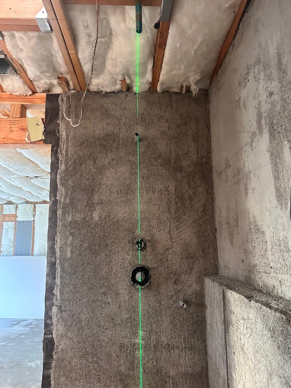 A green laser line marking the layout on a concrete floor, lined up with new drain openings below an open ceiling