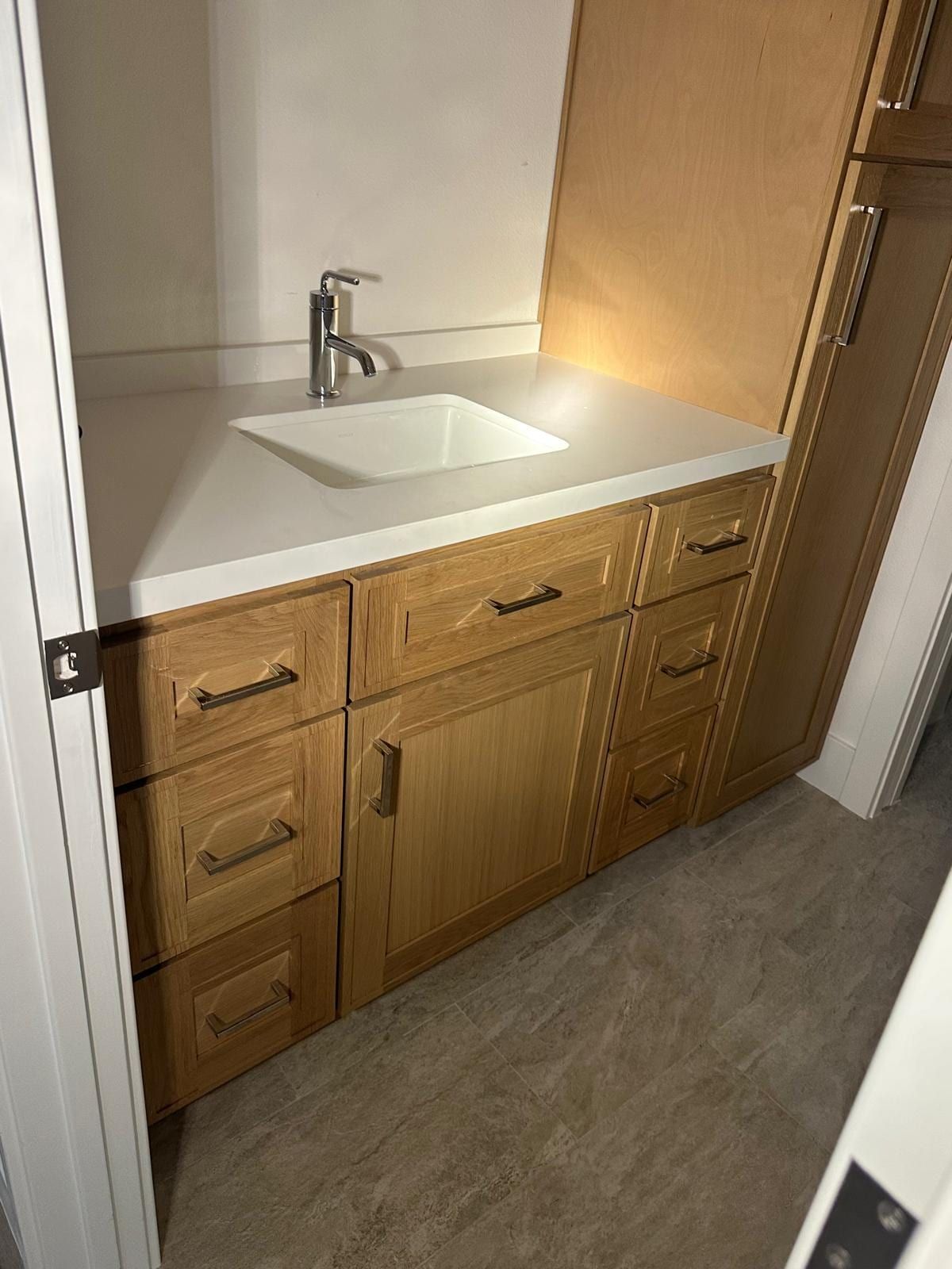 A new vanity with natural wood cabinets and a tall linen cabinet, a white top with an undermount sink and a single-handle faucet